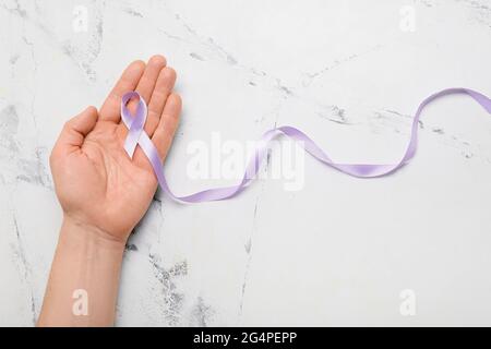 Männliche Hand mit Fliederband auf hellem Hintergrund. Konzept zur Sensibilisierung für Krebs Stockfoto