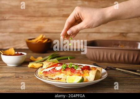 Frau, die auf dem Teller grüne Zwiebel zu leckeren Enchilada gab Stockfoto