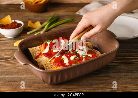 Frau schneidet heiße Enchilada in Backform auf dem Tisch Stockfoto