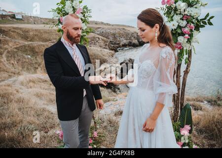 Junge Frauen in einem weißen Kleid legt einen Ring auf den Finger eines Mannes in einem Anzug. Hochzeitszeremonie. Stockfoto