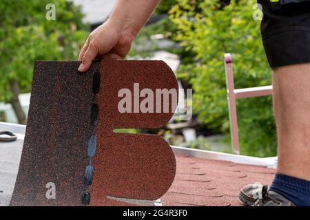 Die Hände des Mitarbeiters sind beim Einbau von Bitumendachschindeln angebracht Stockfoto