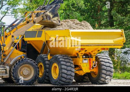 Gelber Frontlader lädt den Sand in den Muldenkipper Stockfoto