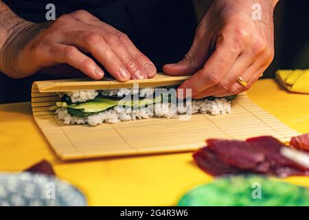 Sushi-Chef dreht Nori-Blatt mit Füllung in der Rolle Nahaufnahme Stockfoto