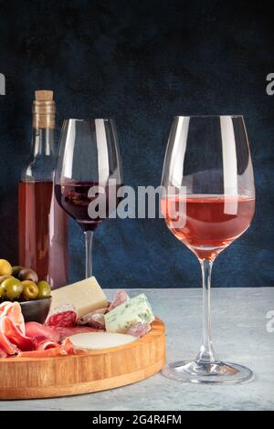 Wein, Käse, Wurstwaren und Oliven. Italienisches Antipasti-Buffet mit Gläsern Rose und Rotwein mit blauem Käse auf dunklem Hintergrund Stockfoto
