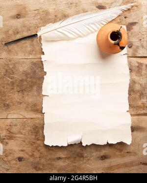 Vintage weißer Federkiel zum Schreiben von leerem Pergamentblatt mit Platz für Text und Tintenfass auf rauem Holztisch Stockfoto