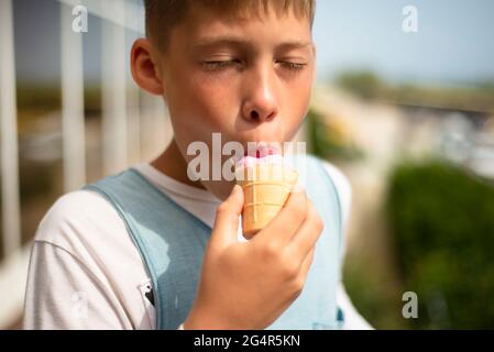 Der Junge isst Eis. Eiscreme mit rosa Erdbeeren in einem Waffelbecher. Genuss an einem heißen Tag. Platz für Text kopieren. Stockfoto