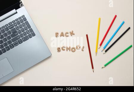 Zurück zur Schule minimalistisches Konzept. Laptop, Farbstifte auf beigefarbenem Hintergrund. Slogan Back School.Draufsicht Stockfoto