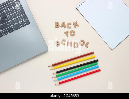 Zurück zur Schule minimalistisches Konzept. Laptop, Farbstifte, Notizbuch auf beigem Hintergrund. Slogan zurück in die Schule mit Holzbuchstaben.Draufsicht Stockfoto