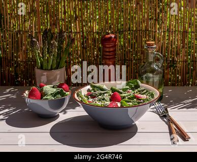 Frische Erdbeeren, grüner Spargel, Feta-Käse, Babyspinat und Rukula-Salat in einer Schüssel mit Mineralwasser serviert. Natürliches Sommerlicht und trendy Stockfoto