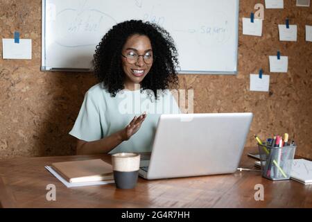 Fröhliche, gemischte Rennen Frau lacht mit Laptop-Videostream-Telefonkonferenz, sehen Sie sich ein Webinar an Stockfoto