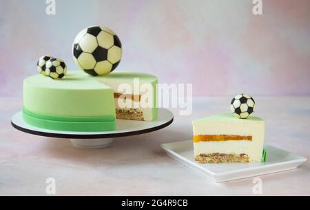 Geburtstagstorte mit Schokoladen-Fußballbällen auf der Oberseite und ein Stück Kuchen mit einem schönen Schnitt liegt auf einem quadratischen Teller - Nahaufnahme und Kopierplatz Stockfoto