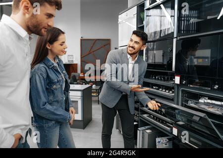 Männliche Verkäuferin hilft jungen Paaren, ein neues Zuhause zu wählen Gerät Stockfoto