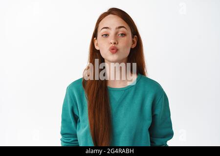 Schöne kaukasische Rotschopf Mädchen küssen, Pucker Lippen und lehnt sich für Kuss, romantische Beziehung oder Datum, flirty vor weißem Hintergrund stehen Stockfoto