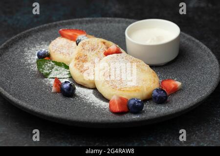 Käsekuchen mit Erdbeeren, Heidelbeeren und saurer Creme auf einem Teller serviert Stockfoto