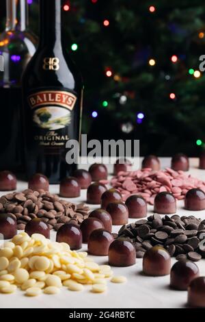 Verschiedene dunkle, milchige, weiße und farbige Schokolade in Kalbskörtchen und Flaschen mit Cremelikör auf dem Hintergrund der Weihnachtsbeleuchtung Stockfoto