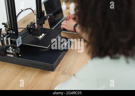 High-Angle-Ansicht junger Designer, die mit 3D-Drucker und Laptop in modernen Büros arbeiten Stockfoto