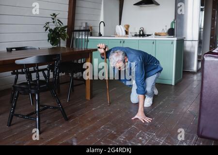 Älterer Mann mit Krücke, der zu Hause auf den Boden fällt Stockfoto