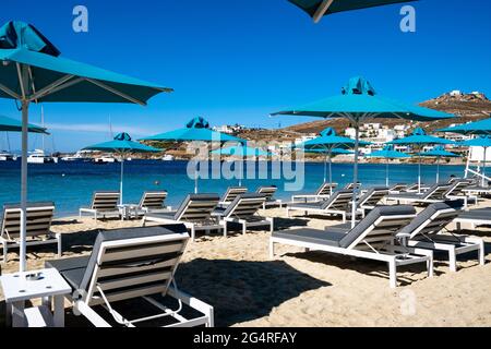 Sonnenschirme und Liegen am Strand bei Ornos. Mykonos, Griechenland. Stockfoto