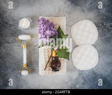 Natürliche, umweltfreundliche, Blumen kosmetische Komposition mit Glas mit natürlicher Gesichtscreme, Serum, wiederverwendbaren Hautpflegezubehör und lila Zweig Stockfoto