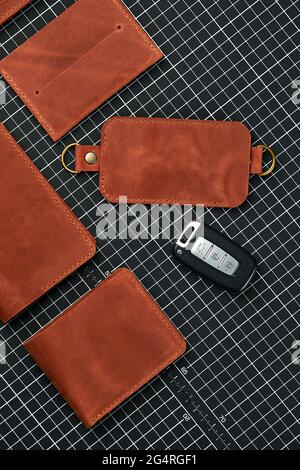 Ein Set aus Geldbörsen, Visitenkartenhaltern und Schlüsselhaltern aus handgefertigtem Leder, aus rotem Leder auf einem Tisch zum Schneiden von Leder, umgeben von To Stockfoto