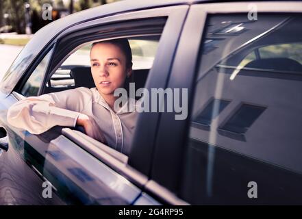 Seriöse Frau im Auto. Traurig, verärgert oder müde Taxifahrer. Coole, elegante Geschäftsfrau, die auf dem Rücksitz sitzt und aus dem Fenster blickt. Stockfoto
