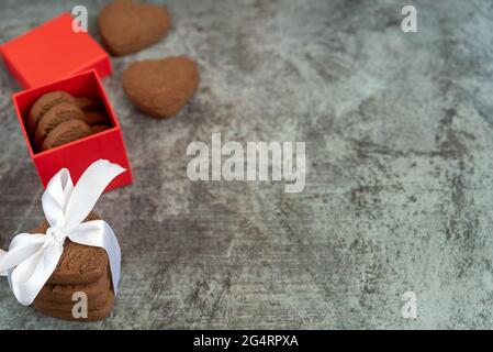 Stapel herzförmiger Shortbread-Kekse mit weißem Band und Geschenkbox auf grauem Hintergrund gebunden Stockfoto