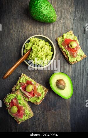 Vollkornbrot mit Avocado-Aufstrich und Prosciutto auf Holzküchentisch Stockfoto