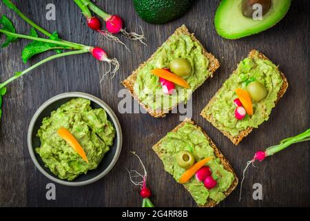 Vollkornbrot mit Avocado-Aufstrich und Gemüse auf einem hölzernen Küchentisch Stockfoto