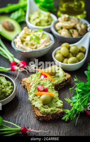 Vollkornbrot mit Avocado-Aufstrich und Gemüse auf einem hölzernen Küchentisch Stockfoto