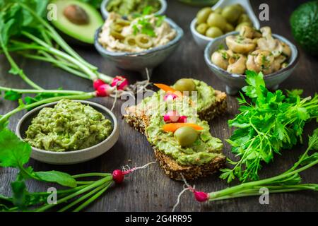 Vollkornbrot mit Avocado-Aufstrich und Gemüse auf einem hölzernen Küchentisch Stockfoto