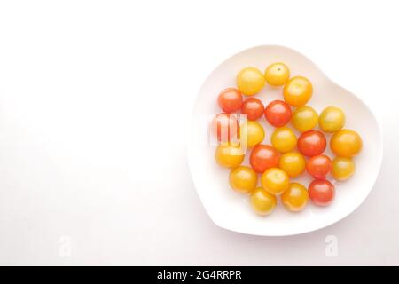 Farbe Kirschtomate auf Herz-Form-Platte auf weißem Hintergrund Stockfoto