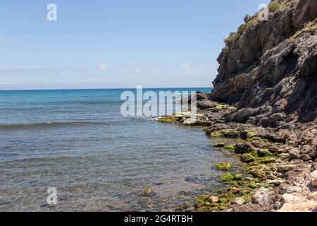 Felsen und Klippen von unten gesehen am Rand eines Meeres aus transparentem Wasser an der spanischen Mittelmeerküste. Stockfoto