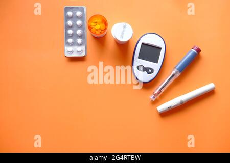 Insulin-Stift, diabetische Messgeräte und Pillen auf orangefarbenem Hintergrund Stockfoto