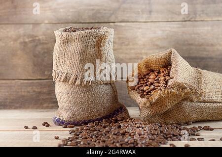 Gerösteter Kaffee in zwei Beuteln auf Holzboden. Kaffeebohnen sind in den Hintergrund gefallen. Kaffeegeschäft. Kaffee ernten. Copyspace Stockfoto