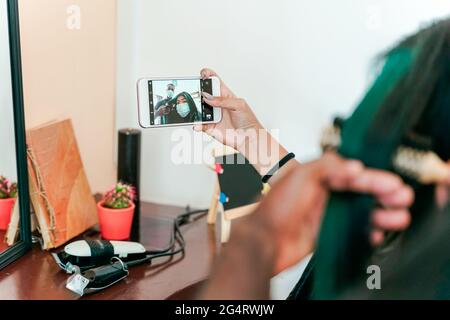 Asiatische Mädchen machen Selfie, während Friseur kämmen ihr Haar. Frau und Friseur mit Schutzmaske für Coronavirus Zeit. Stockfoto