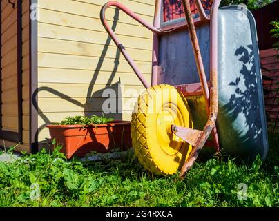 Gartenwagen mit gelbem Rad, der an einem sonnigen Sommertag im Garten auf grünem Gras geparkt ist. Stockfoto