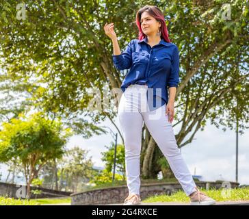 Junge Latina-Frau, die im Park steht und auf ihre rechte Hand schaut Stockfoto