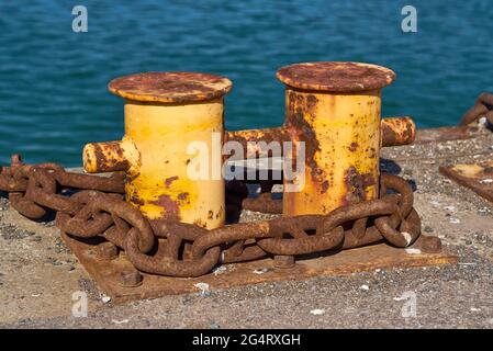 Seitenansicht eines doppelbittigen Pollers mit einer schweren Kette um ihn herum. Stockfoto