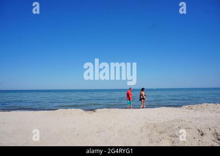 POBIEROWO, POLEN - 07. Jun 2021: Menschen, die an einem warmen Frühlingstag am Sandstrand entlang des Wassers spazieren. Stockfoto
