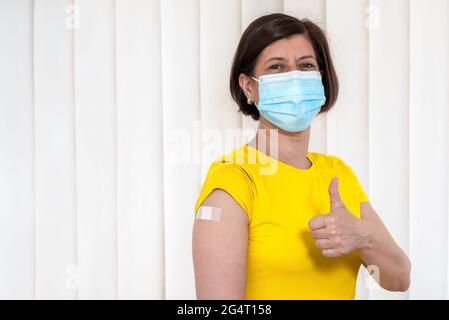 Porträt einer Frau in OP-Maske, die nach einer Impfung gegen Coronavirus den Daumen nach oben gestikuliert hat. Covid-19-Impfung. Stockfoto