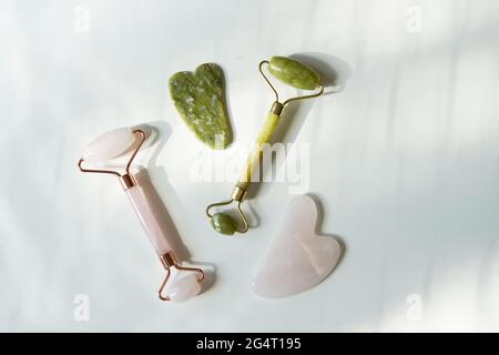 Gesichtswalze und Gua Sha Massagegerät aus Natursteinen auf weißem Tisch mit Schatten Stockfoto