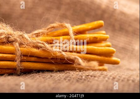 Brotstangen mit Salz, gebunden mit Garn auf dem Hintergrund eines selbstgewebten Stoffes mit einer rauen Textur. Nahaufnahme Selektiver Fokus Stockfoto