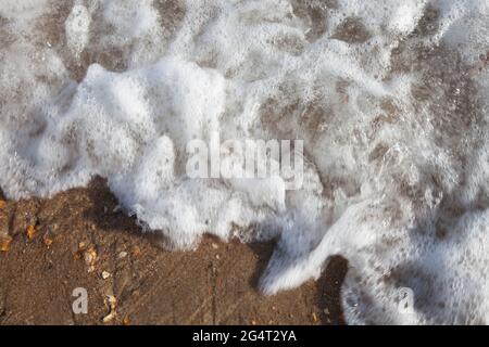 Nahaufnahme von kleinen Wellen, die am Strand brechen und Blasen und Schaum erzeugen Stockfoto