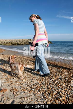 Frau und treuer Orangen-Cocker-Spaniel, die am Strand, am Meer spazieren gehen Stockfoto