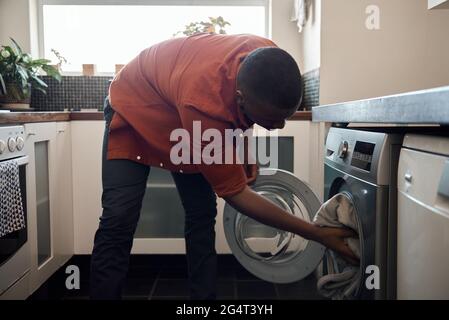 Junger afrikanischer Mann, der in seiner Küche Kleidung wäscht Stockfoto