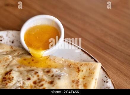 Köstlicher Pfannkuchen gefüllt mit Nüssen und Honig, der wunderschön auf weißem und braunem Keramikplatte auf Holztischhintergrund herabrieselt. Nahaufnahme. Kopie en Stockfoto