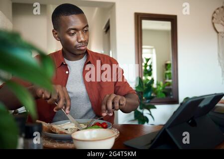 Afrikanischer Mann, der beim Frühstück etwas auf einem digitalen Tablet sieht Stockfoto