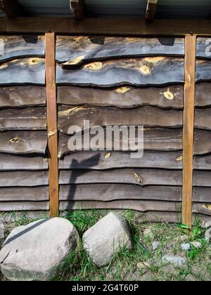 Formatfüllende Ansicht einer Wand aus horizontal überlappenden und ungetrimmten Brettern mit zwei vertikalen Säulen zur Stabilisierung des Außenbereichs. Stockfoto