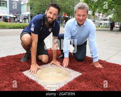 23. Juni 2021, Sachsen-Anhalt, Magdeburg: Bennett Wiegert (l), Trainer des Handball-Bundesligisten SC Magdeburg, und Lutz Trümper, Oberbürgermeister von Magdeburg, hocken vor der Granitbronze-Skulptur 'Sports Walk of Fame', die die EHF-Europameister des SC Magdeburg heute enthüllen durften. Der SC Magdeburg hatte im Mai den Titel der EHF-Europaliga geholt. Die in den Bordstein eingebettete und dem „Walk of Fame“ in Hollywood nachempfundene Plakette soll diesen Erfolg und viele andere sportliche Spitzenleistungen der Handball-Bundesliga würdigen. Der „Sports Walk of Fame“, whi Stockfoto