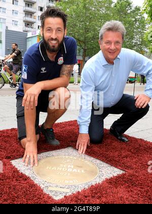 23. Juni 2021, Sachsen-Anhalt, Magdeburg: Bennett Wiegert (l), Trainer des Handball-Bundesligisten SC Magdeburg, und Lutz Trümper, Oberbürgermeister von Magdeburg, hocken vor der Granitbronze-Skulptur 'Sports Walk of Fame', die die EHF-Europameister des SC Magdeburg heute enthüllen durften. Der SC Magdeburg hatte im Mai den Titel der EHF-Europaliga geholt. Die in den Bordstein eingebettete und dem „Walk of Fame“ in Hollywood nachempfundene Plakette soll diesen Erfolg und viele andere sportliche Spitzenleistungen der Handball-Bundesliga würdigen. Der „Sports Walk of Fame“, whi Stockfoto